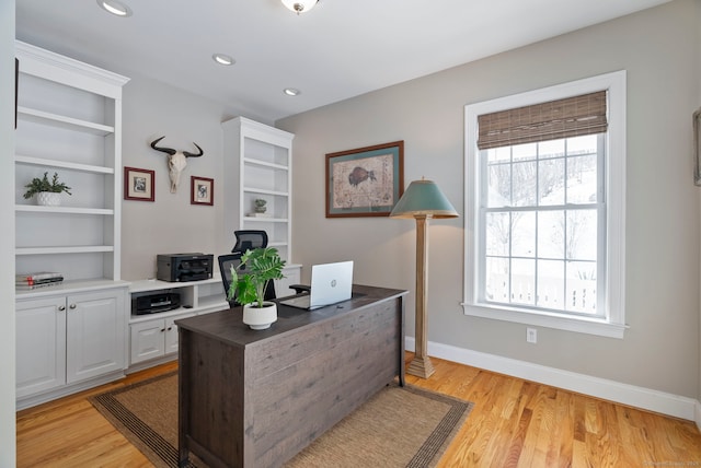 office area with a wealth of natural light, light hardwood / wood-style floors, and built in shelves