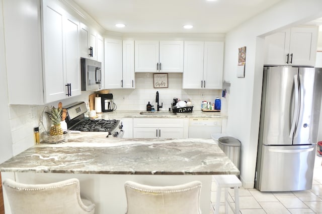 kitchen with appliances with stainless steel finishes, sink, white cabinets, a kitchen breakfast bar, and light stone countertops