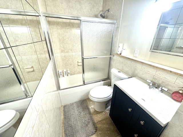 full bathroom with bath / shower combo with glass door, tile walls, vanity, and toilet