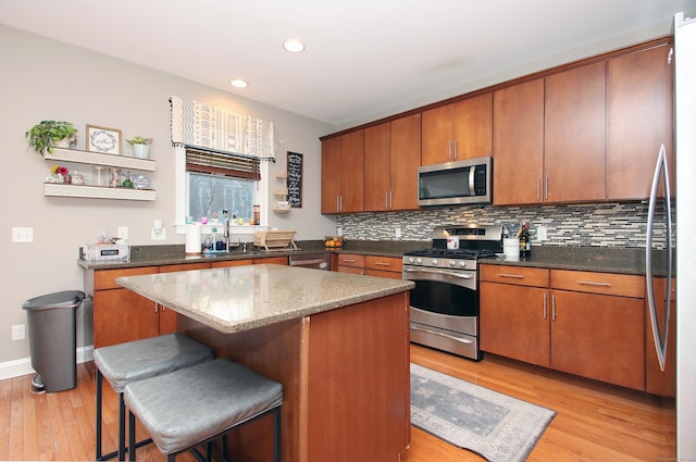 kitchen with a breakfast bar area, appliances with stainless steel finishes, tasteful backsplash, a kitchen island, and light wood-type flooring