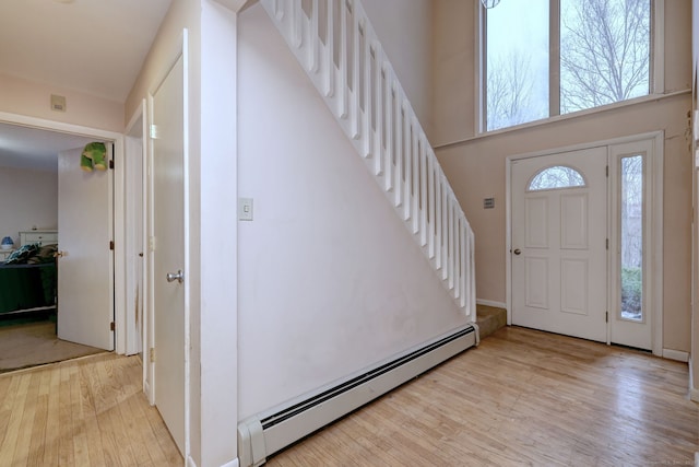 entryway featuring a towering ceiling, a baseboard radiator, and light wood-type flooring