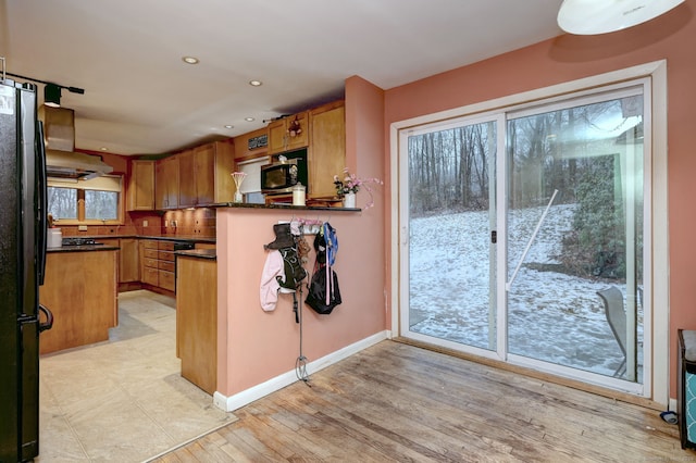 kitchen featuring black fridge, kitchen peninsula, light wood-type flooring, and exhaust hood