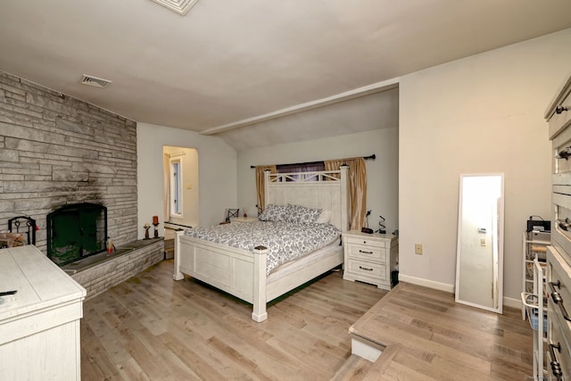 bedroom with lofted ceiling, light wood-type flooring, and a fireplace