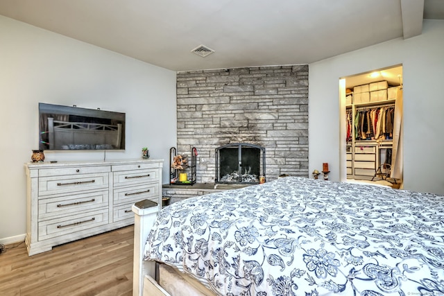 bedroom with a walk in closet, a fireplace, and light wood-type flooring