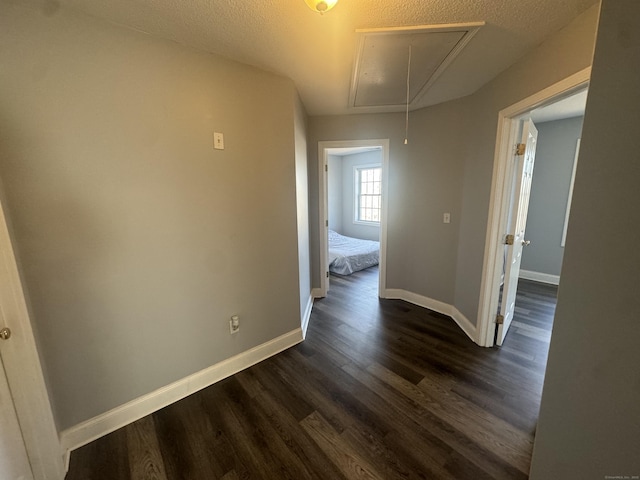 corridor with attic access, dark wood-style floors, baseboards, and a textured ceiling