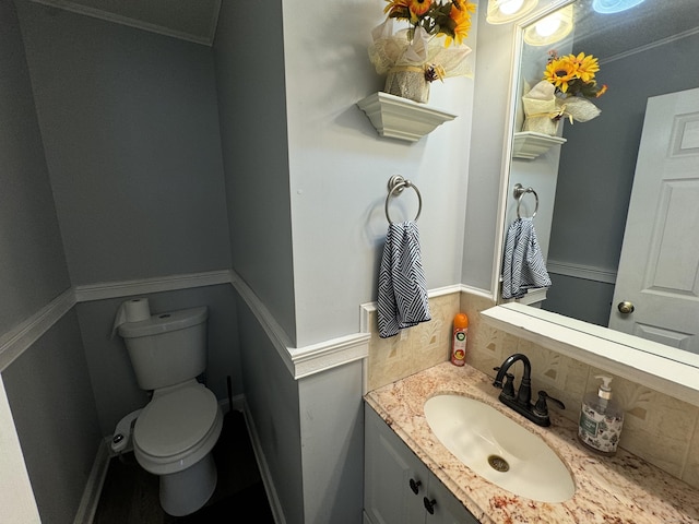 half bath featuring decorative backsplash, toilet, vanity, and ornamental molding