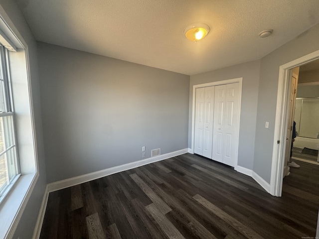 unfurnished bedroom with visible vents, a textured ceiling, dark wood-style floors, a closet, and baseboards