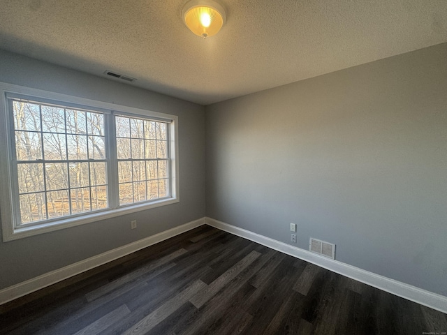 unfurnished room featuring dark wood-style floors, visible vents, a textured ceiling, and baseboards