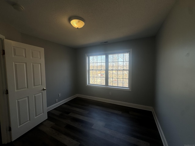 spare room with visible vents, baseboards, a textured ceiling, and dark wood-style flooring