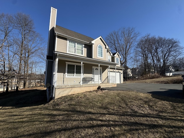 view of front of home featuring a porch, a chimney, driveway, and a front yard