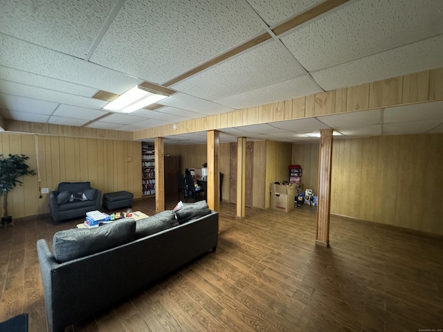 living area with a paneled ceiling, wood finished floors, and wood walls