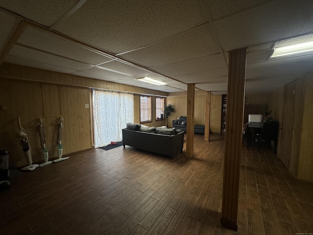 living area featuring wooden walls, a paneled ceiling, and dark wood-style flooring