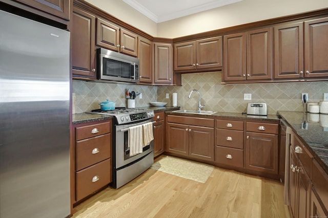 kitchen featuring sink, crown molding, light hardwood / wood-style flooring, dark stone countertops, and stainless steel appliances