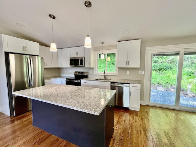 kitchen with appliances with stainless steel finishes, decorative light fixtures, white cabinets, a center island, and light stone counters