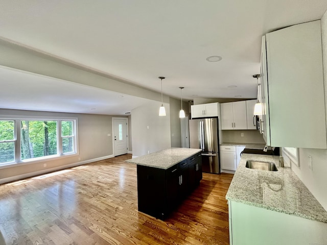 kitchen featuring decorative light fixtures, a center island, stainless steel refrigerator, light stone countertops, and white cabinets