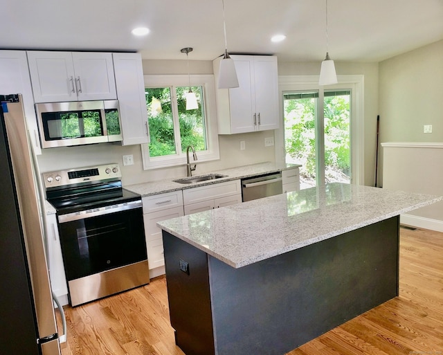 kitchen with sink, white cabinetry, decorative light fixtures, appliances with stainless steel finishes, and a kitchen island