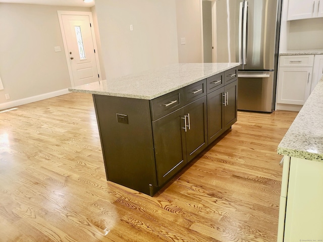 kitchen with dark brown cabinetry, white cabinetry, light stone countertops, and stainless steel refrigerator