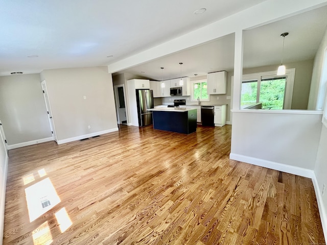 kitchen with hanging light fixtures, appliances with stainless steel finishes, a kitchen island, light hardwood / wood-style floors, and white cabinets