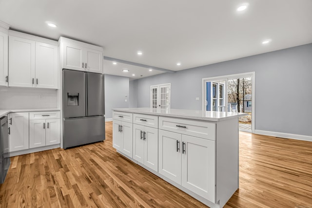 kitchen featuring appliances with stainless steel finishes, white cabinetry, a center island, light stone countertops, and light hardwood / wood-style floors