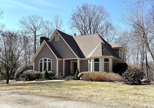 view of front of property featuring roof with shingles, a chimney, and a front lawn