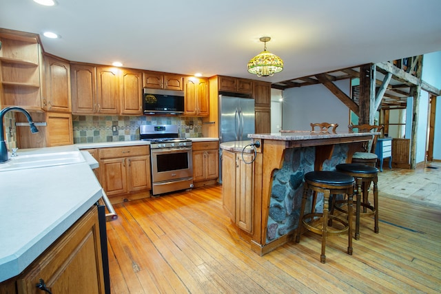 kitchen featuring sink, hanging light fixtures, light hardwood / wood-style flooring, appliances with stainless steel finishes, and a kitchen island