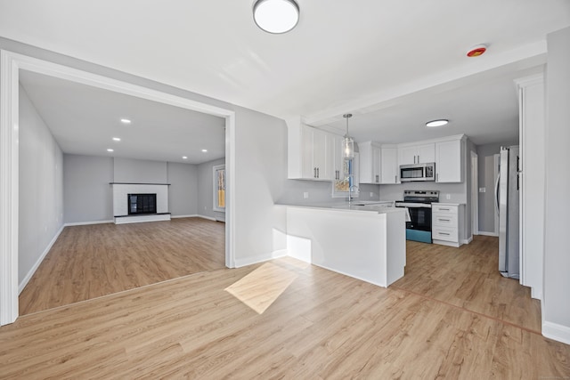 kitchen featuring a fireplace, white cabinetry, hanging light fixtures, kitchen peninsula, and stainless steel appliances