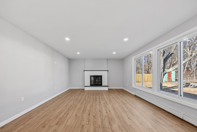 unfurnished living room with baseboard heating, a brick fireplace, and light hardwood / wood-style flooring