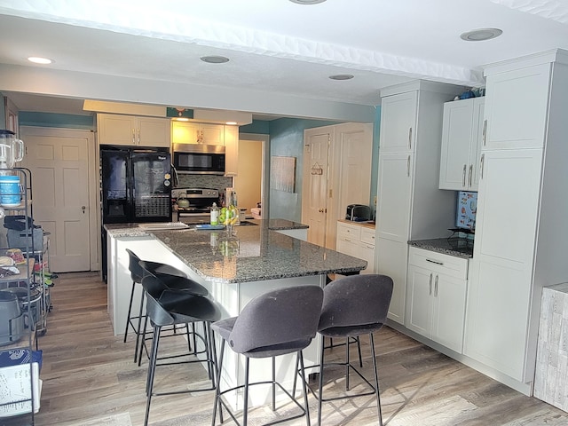 kitchen featuring stainless steel appliances, a kitchen island, a breakfast bar area, and dark stone countertops