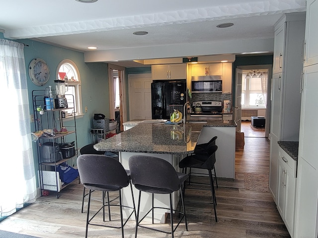 kitchen featuring a breakfast bar area, tasteful backsplash, stainless steel electric range oven, black refrigerator, and hardwood / wood-style flooring