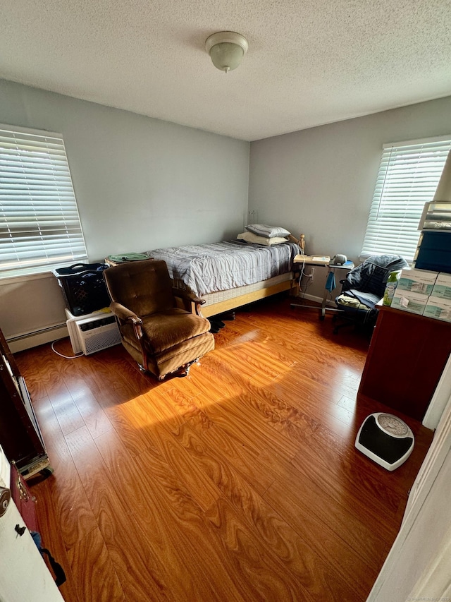 bedroom with wood-type flooring, a textured ceiling, and a baseboard heating unit