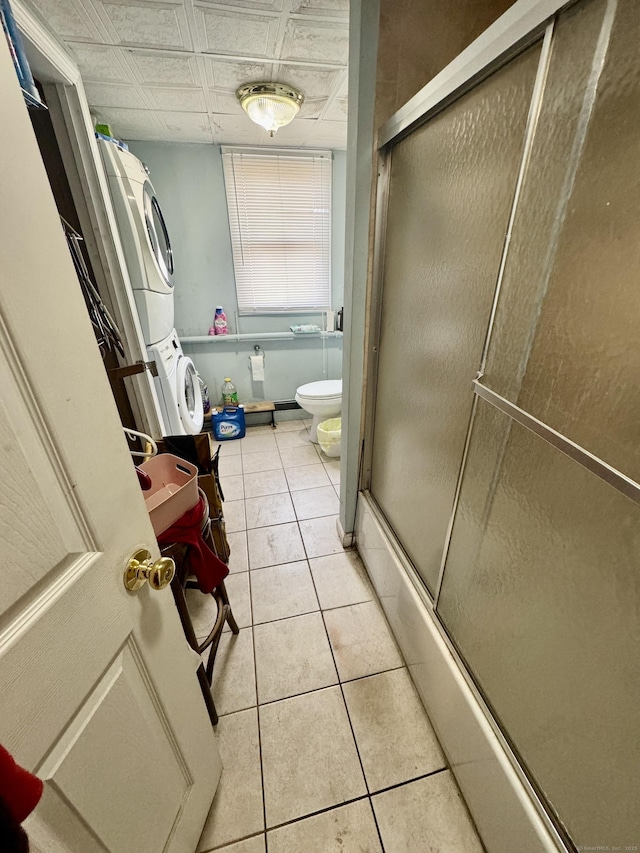 bathroom featuring combined bath / shower with glass door, stacked washer / drying machine, tile patterned floors, and toilet