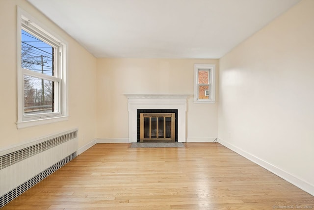 unfurnished living room with plenty of natural light, radiator heating unit, and light wood-type flooring