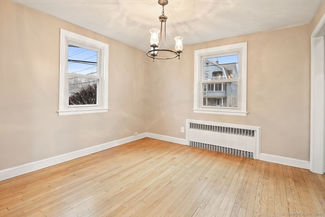 unfurnished room featuring an inviting chandelier, radiator heating unit, and light hardwood / wood-style floors