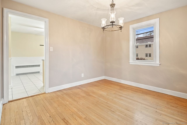 empty room with light hardwood / wood-style flooring, a notable chandelier, and radiator heating unit