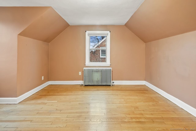 additional living space with vaulted ceiling, radiator heating unit, and light wood-type flooring