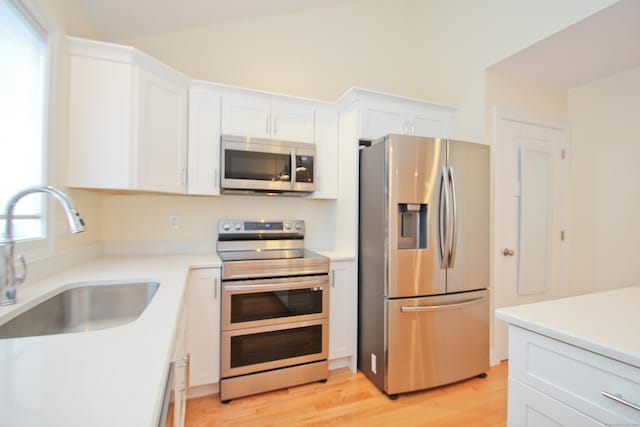 kitchen featuring vaulted ceiling, white cabinetry, sink, light hardwood / wood-style floors, and stainless steel appliances