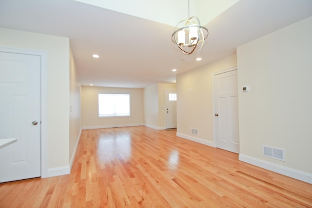 spare room with a notable chandelier and light wood-type flooring