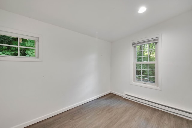 empty room featuring a baseboard radiator, recessed lighting, baseboards, and wood finished floors