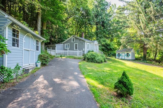 view of front of house with aphalt driveway, an outdoor structure, fence, a front lawn, and a chimney