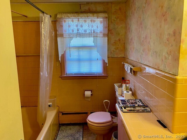 bathroom with toilet, a healthy amount of sunlight, tile walls, and shower / bath combo with shower curtain