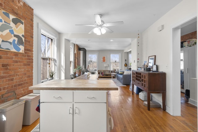 kitchen with white cabinetry, butcher block counters, a wealth of natural light, light hardwood / wood-style floors, and a wood stove