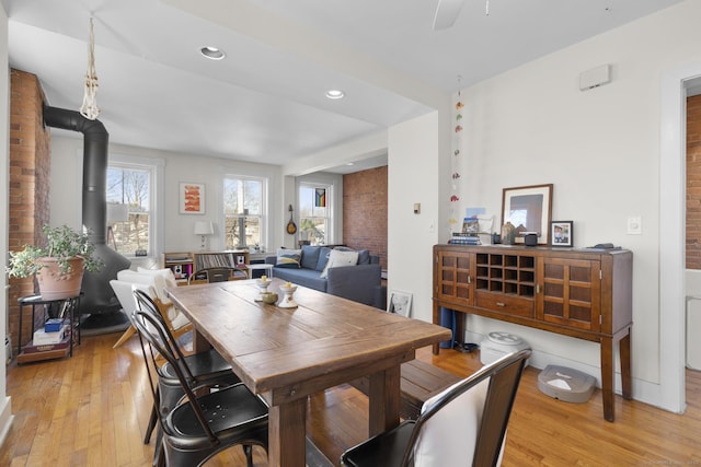 dining room featuring brick wall, a wood stove, ceiling fan, and light hardwood / wood-style flooring