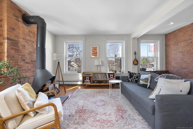 living room featuring brick wall, a wood stove, light wood-type flooring, and baseboard heating