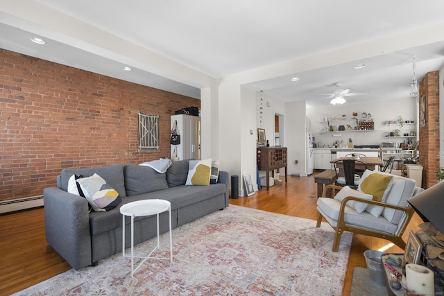 living room with ceiling fan, brick wall, a baseboard heating unit, and light wood-type flooring