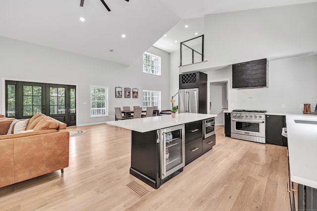 kitchen with wine cooler, high end appliances, a center island, light hardwood / wood-style flooring, and a towering ceiling