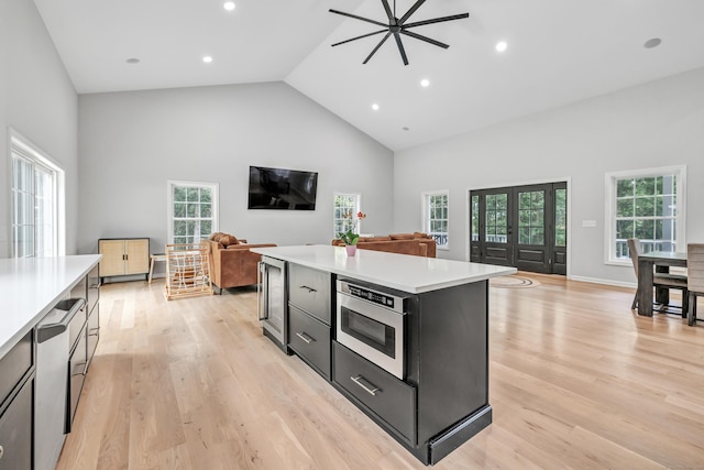 kitchen featuring stainless steel microwave, high vaulted ceiling, light hardwood / wood-style floors, and a kitchen island