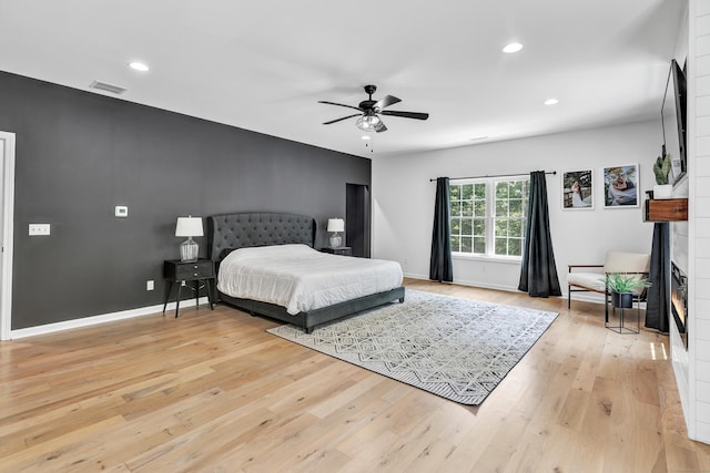 bedroom with ceiling fan, a fireplace, and light hardwood / wood-style flooring