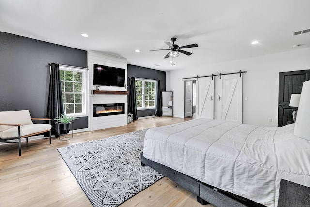 bedroom with ceiling fan, a fireplace, a barn door, and light hardwood / wood-style flooring