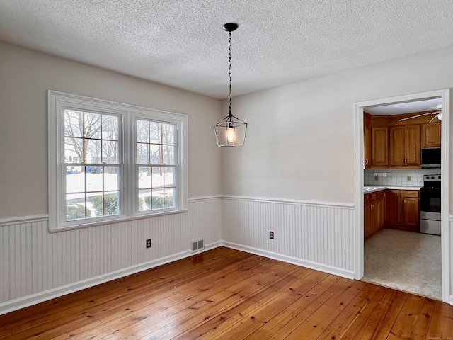 unfurnished dining area featuring ceiling fan, a textured ceiling, and light hardwood / wood-style floors