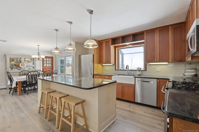 kitchen featuring a kitchen island, decorative light fixtures, sink, stainless steel appliances, and light hardwood / wood-style flooring